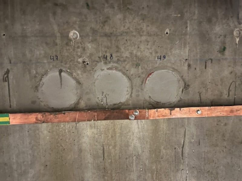 Drie gerepareerde cirkelvormige plekken op een betonnen muur, gemarkeerd met 47, 48 en 49, boven een horizontale metalen balk: precies het soort probleem dat een vochtbestrijdingsexpert of een specialist in waterdichting en betoninjectie kan oplossen.